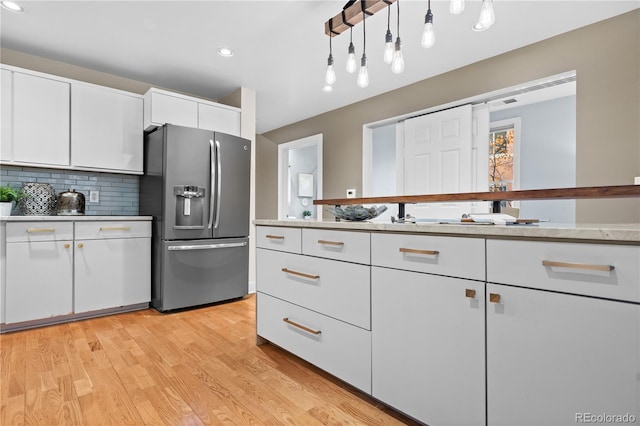 kitchen with stainless steel fridge with ice dispenser, decorative backsplash, light countertops, light wood-style floors, and white cabinetry