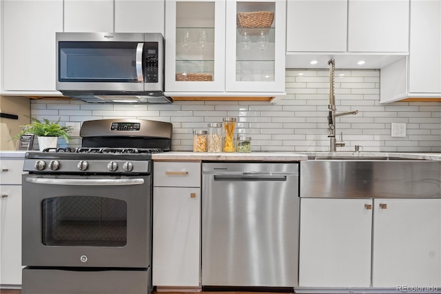 kitchen with glass insert cabinets, light countertops, decorative backsplash, appliances with stainless steel finishes, and white cabinetry