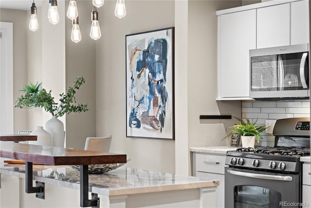 kitchen featuring decorative backsplash, hanging light fixtures, white cabinetry, and appliances with stainless steel finishes