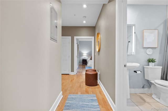 corridor featuring recessed lighting, baseboards, electric panel, and light wood-style flooring