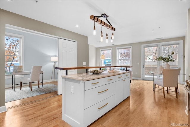 kitchen featuring white cabinetry, decorative light fixtures, light wood-style floors, and a center island