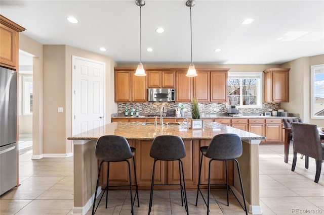 kitchen with appliances with stainless steel finishes, decorative light fixtures, sink, a kitchen island with sink, and light stone counters