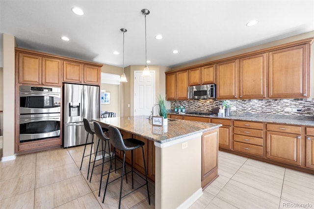 kitchen with light stone countertops, stainless steel appliances, sink, hanging light fixtures, and a center island with sink