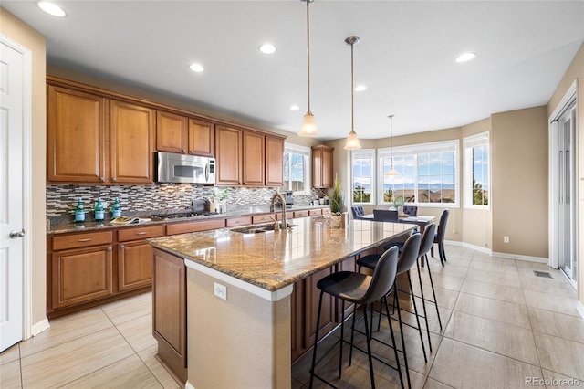 kitchen with decorative light fixtures, sink, a kitchen island with sink, stainless steel appliances, and light stone counters