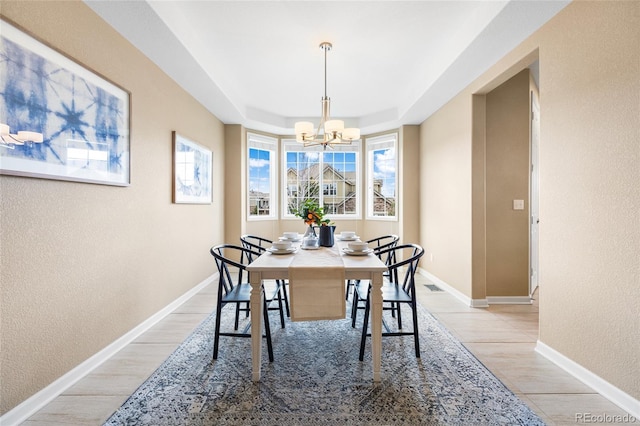 dining area featuring light hardwood / wood-style flooring, a tray ceiling, and a notable chandelier