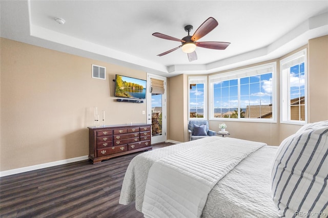 bedroom with dark wood-type flooring, ceiling fan, and a tray ceiling