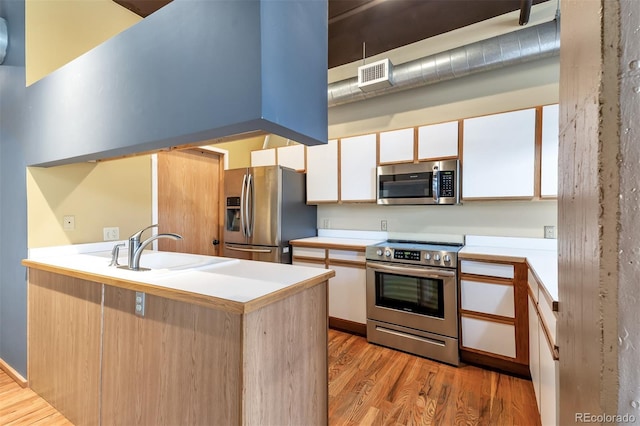 kitchen featuring white cabinetry, appliances with stainless steel finishes, kitchen peninsula, and light hardwood / wood-style floors