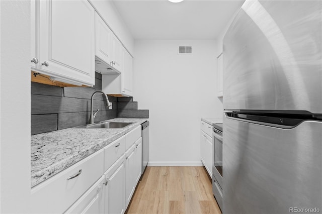 kitchen with appliances with stainless steel finishes, light wood-type flooring, tasteful backsplash, sink, and white cabinets