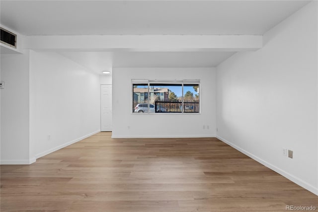 empty room with beam ceiling and light wood-type flooring