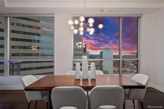 dining room with a city view, visible vents, wood finished floors, a chandelier, and baseboards