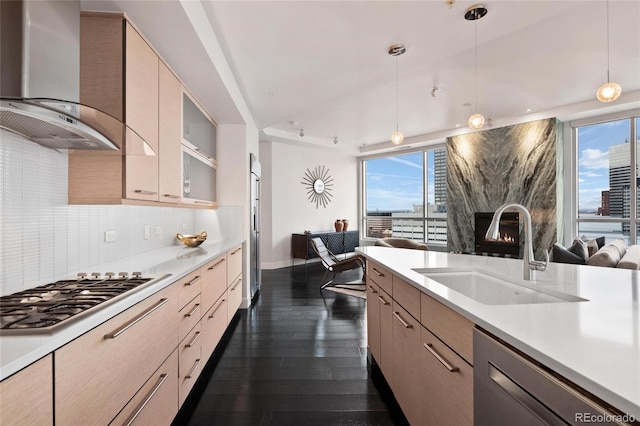 kitchen with appliances with stainless steel finishes, open floor plan, light countertops, wall chimney range hood, and a sink