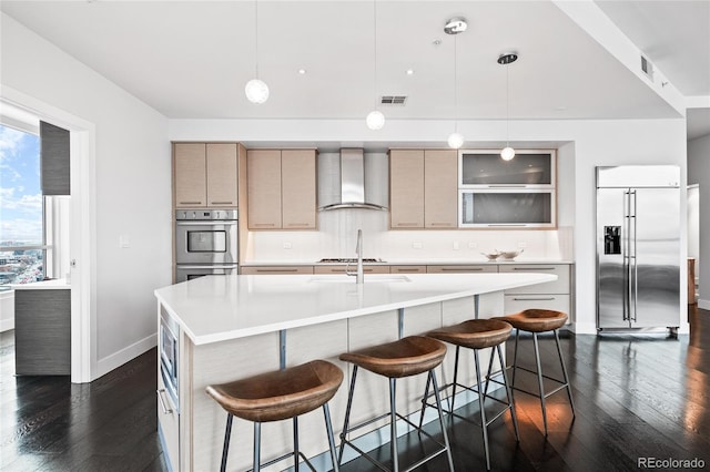 kitchen featuring wall chimney range hood, dark wood finished floors, stainless steel appliances, and light countertops