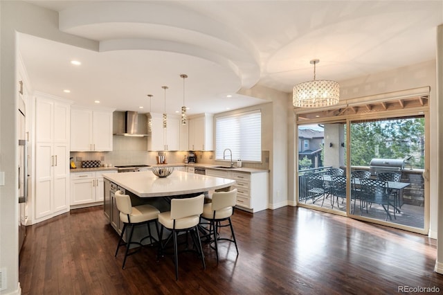 kitchen with pendant lighting, wall chimney range hood, sink, and a center island