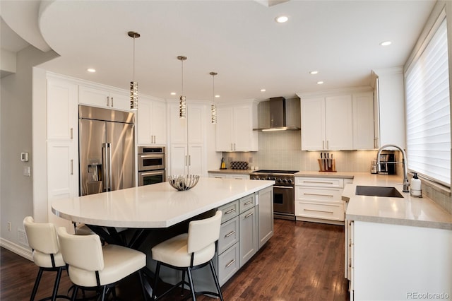 kitchen with pendant lighting, sink, high end appliances, a center island, and wall chimney range hood