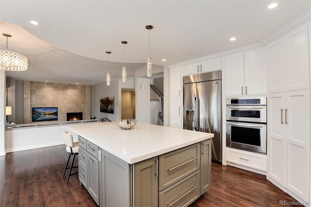 kitchen featuring appliances with stainless steel finishes, white cabinets, a kitchen bar, hanging light fixtures, and a center island