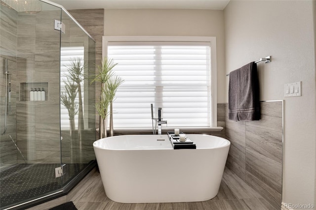 bathroom with a healthy amount of sunlight, independent shower and bath, and tile walls