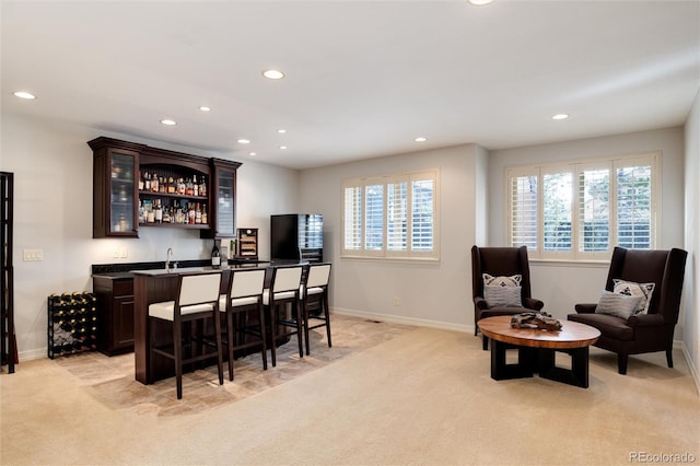 bar featuring dark brown cabinetry, sink, and light colored carpet