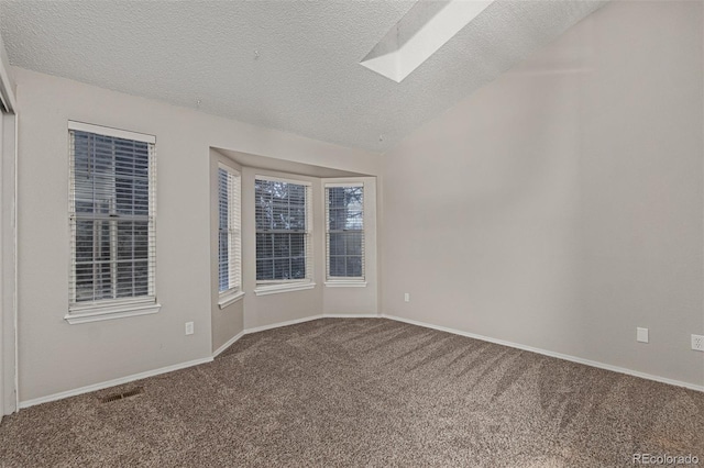 carpeted spare room with vaulted ceiling with skylight, visible vents, baseboards, and a textured ceiling