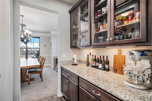 bar featuring carpet floors, a notable chandelier, dark brown cabinetry, light stone countertops, and ornamental molding