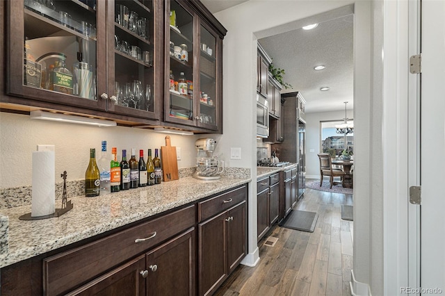 bar with stainless steel microwave, dark brown cabinetry, light stone countertops, a textured ceiling, and dark hardwood / wood-style flooring