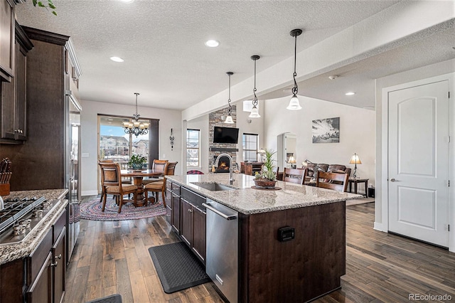 kitchen with a kitchen island with sink, light stone counters, stainless steel appliances, and dark brown cabinetry