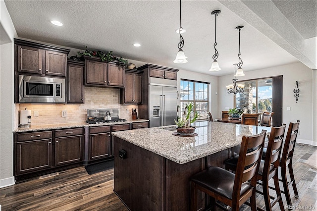 kitchen with a chandelier, pendant lighting, dark brown cabinets, and built in appliances