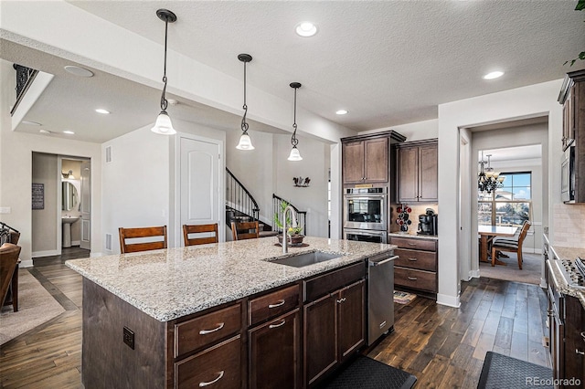 kitchen featuring an island with sink, appliances with stainless steel finishes, decorative light fixtures, light stone countertops, and sink