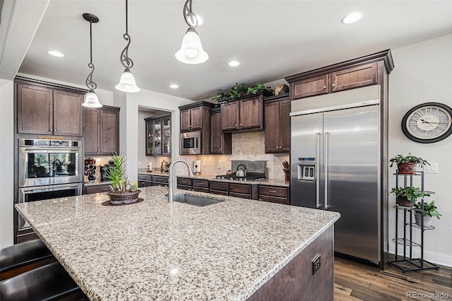 kitchen with decorative light fixtures, an island with sink, and built in appliances