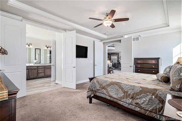 bedroom featuring ceiling fan, ensuite bathroom, a raised ceiling, ornamental molding, and light carpet