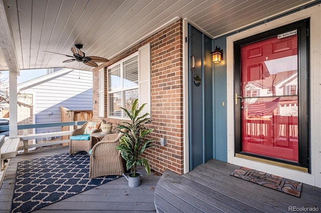 view of exterior entry with a porch, brick siding, and ceiling fan