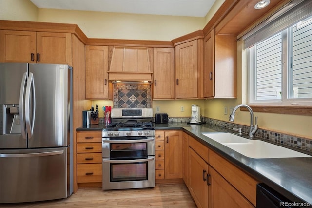 kitchen featuring stainless steel appliances, dark countertops, a sink, light wood-type flooring, and premium range hood