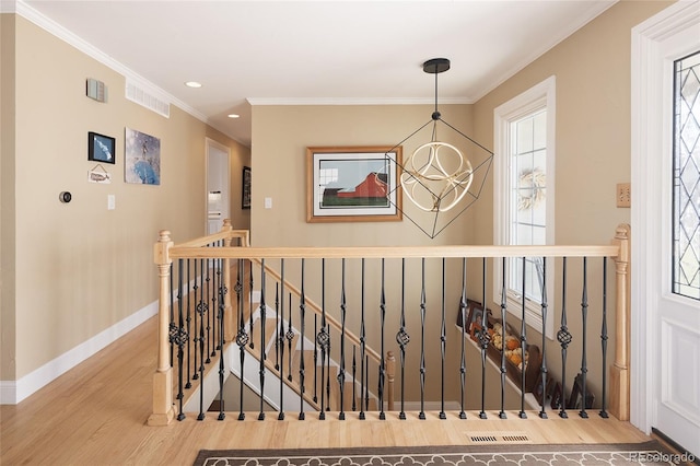 hall with wood finished floors, baseboards, an inviting chandelier, ornamental molding, and an upstairs landing