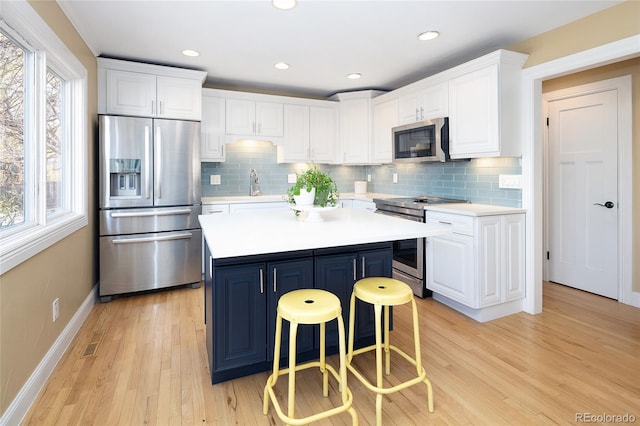 kitchen featuring light countertops, light wood-style flooring, appliances with stainless steel finishes, a kitchen breakfast bar, and white cabinetry