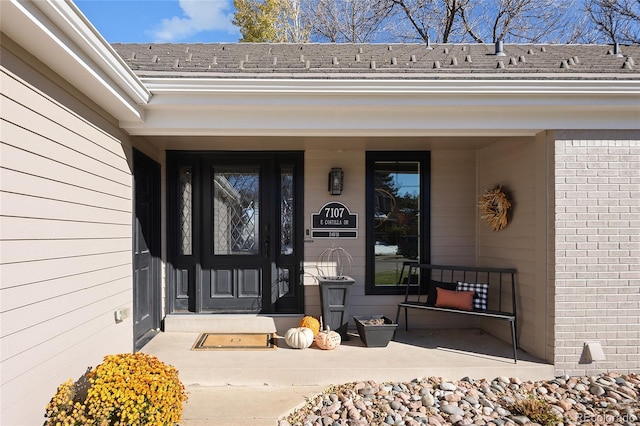 doorway to property with brick siding and roof with shingles