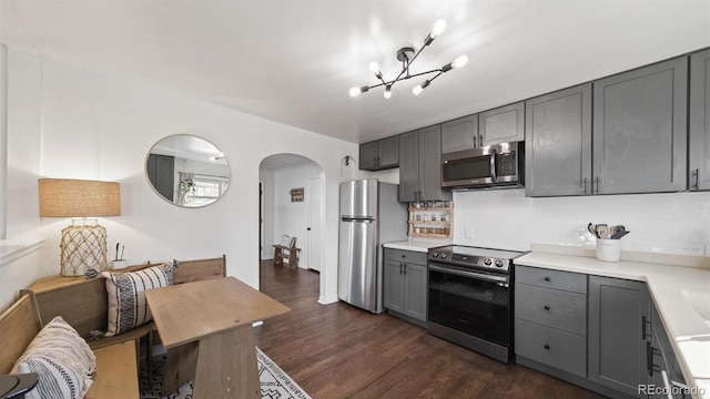 kitchen featuring gray cabinetry, stainless steel appliances, dark wood-type flooring, an inviting chandelier, and backsplash