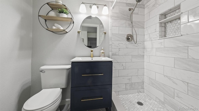 bathroom with toilet, tiled shower, and vanity