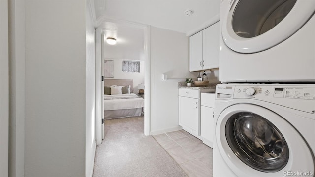 laundry room featuring cabinets, light tile patterned flooring, and stacked washer / dryer