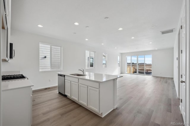 kitchen with light wood-type flooring, stainless steel appliances, sink, a center island with sink, and white cabinets