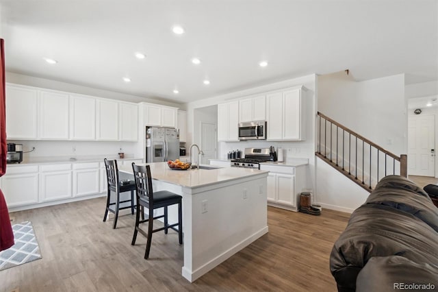 kitchen with stainless steel appliances, a sink, light wood-type flooring, a center island with sink, and a kitchen bar