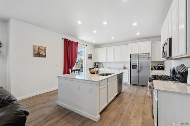 kitchen with stainless steel appliances, a sink, white cabinets, light wood-style floors, and light countertops