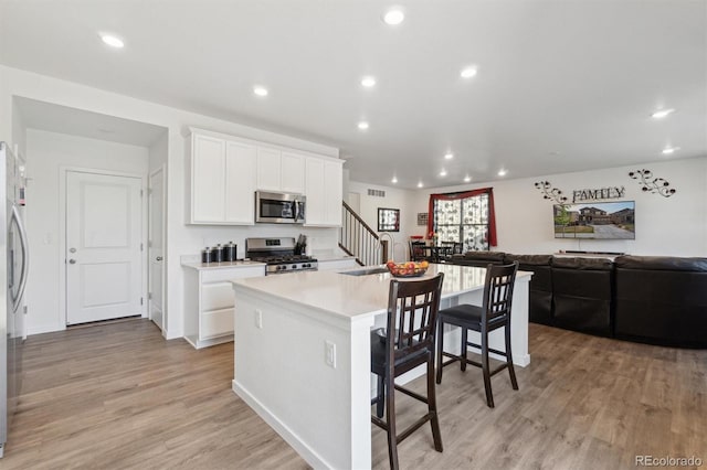 kitchen featuring appliances with stainless steel finishes, open floor plan, a kitchen island with sink, white cabinetry, and recessed lighting