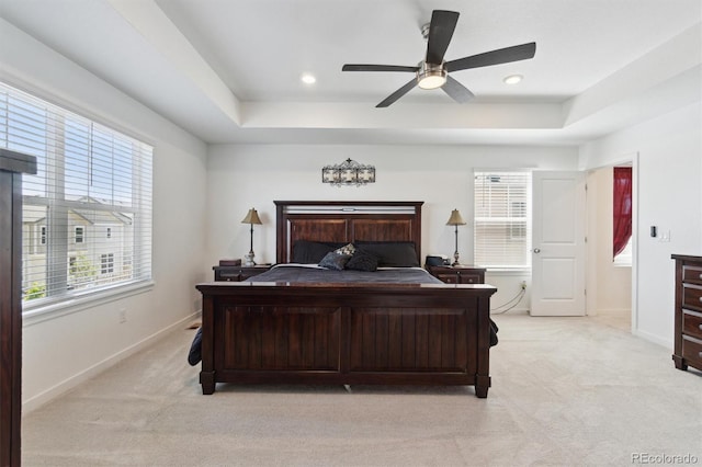 bedroom featuring light carpet, a tray ceiling, and baseboards