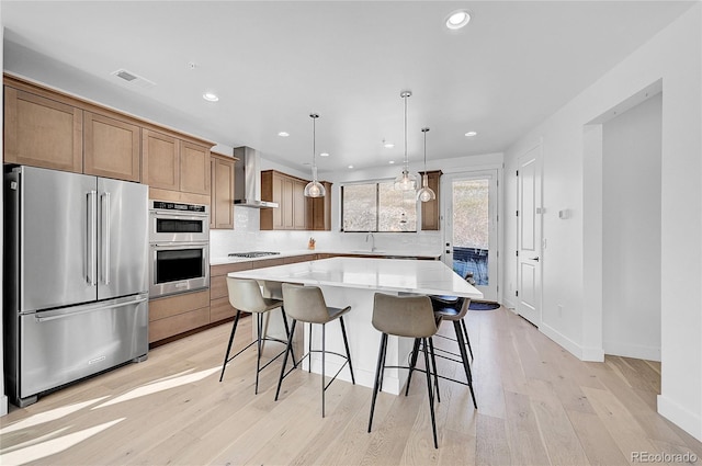 kitchen with a center island, wall chimney exhaust hood, decorative light fixtures, light hardwood / wood-style floors, and stainless steel appliances