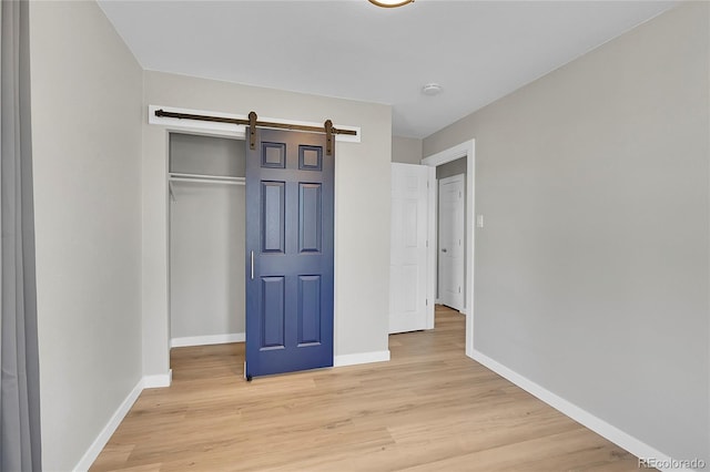 unfurnished bedroom with a barn door, a closet, and light wood-type flooring