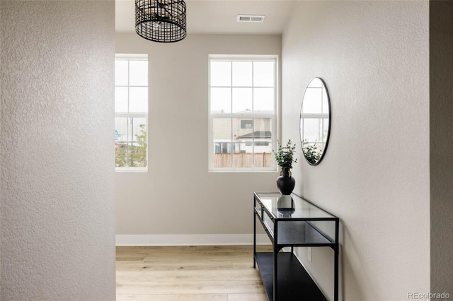 corridor featuring a textured wall, wood finished floors, plenty of natural light, baseboards, and a chandelier