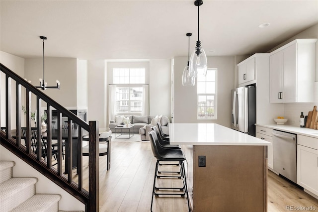 kitchen with stainless steel appliances, a chandelier, light wood finished floors, white cabinets, and a kitchen island