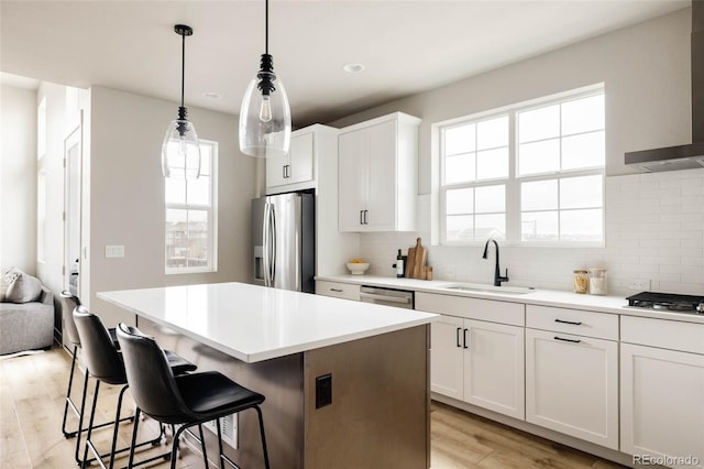 kitchen with appliances with stainless steel finishes, a sink, wall chimney exhaust hood, a center island, and light wood-style floors