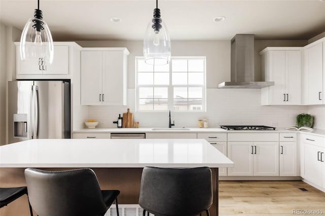 kitchen with wall chimney range hood, a sink, light countertops, a breakfast bar area, and recessed lighting