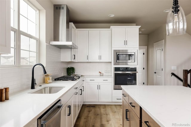 kitchen with stainless steel appliances, wall chimney range hood, a sink, light countertops, and light wood-type flooring