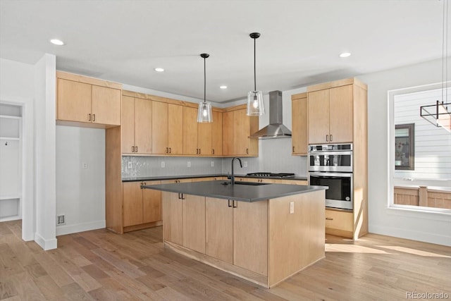 kitchen featuring decorative light fixtures, an island with sink, wall chimney exhaust hood, and light brown cabinets